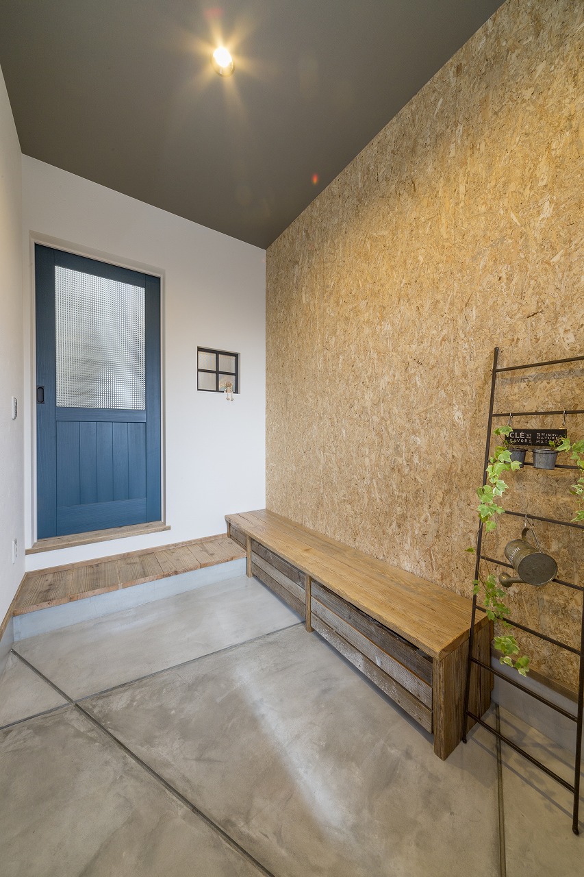 玄関の床はコンクリート、壁はOSBボードで仕上げ、下部収納つきの足場板のベンチをオーダー。